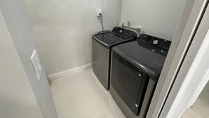 A laundry room with two stacked washers and dryers, a power outlet, and a light switch on the wall.