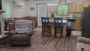 A spacious living area with a wooden ceiling, a dining table, two sofas, and a kitchen area with wooden cabinets and a refrigerator.