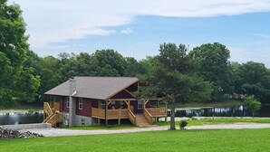 A lodge with a wooden deck and a stone foundation, located near a lake.