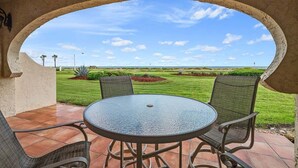 A patio with a round table and two chairs, an archway, and a view of a well-maintained lawn and distant landscape. - Fall Deals + Snowbird Rates | Ocean Views + Beach Getaway (Flagler Beach)