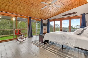 A spacious bedroom with a large bed, a rocking chair, and a view of the outdoors through large windows. - Highland Cattle Farm Cozy Suite - B (Loudon)