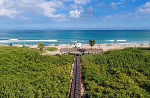 Una playa con vista despejada al océano, un camino que conduce a la playa y una estructura con techo de paja.