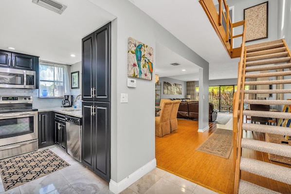 A modern kitchen with stainless steel appliances, a wooden staircase, and a dining area with a view of the outdoors. - Townhouse at Palm Beach Shores Azul (West Palm Beach)