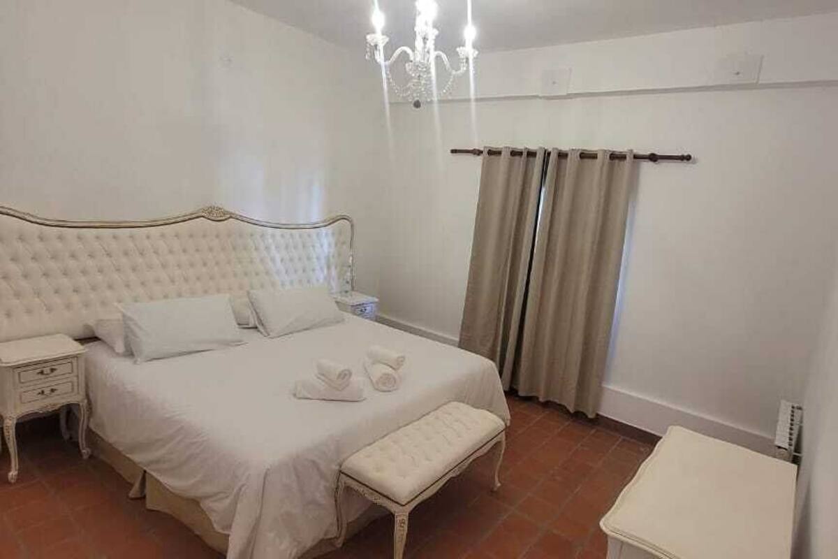 Un dormitorio con cama, mesitas de noche, un banco y una pequeña mesa.