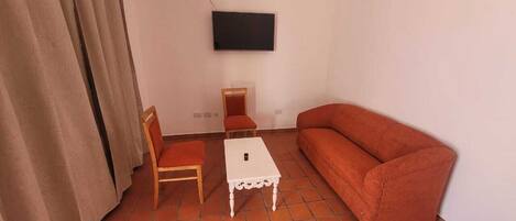 Een woonkamer met een rode bank, een houten stoel, een klein wit tafeltje en een televisie die aan de muur is bevestigd.