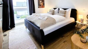 A modern bedroom with a large bed, a bedside table with a lamp, and a view of the street through the window. - Apartment in Winterberg Near Ski Lift & Sauna (Winterberg)