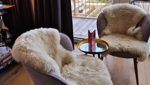 A room with two chairs covered in white fur, a small round table with a book, and a Monopoly board game on a shelf. - Apartment in Winterberg Near Ski Lift & Sauna (Winterberg)