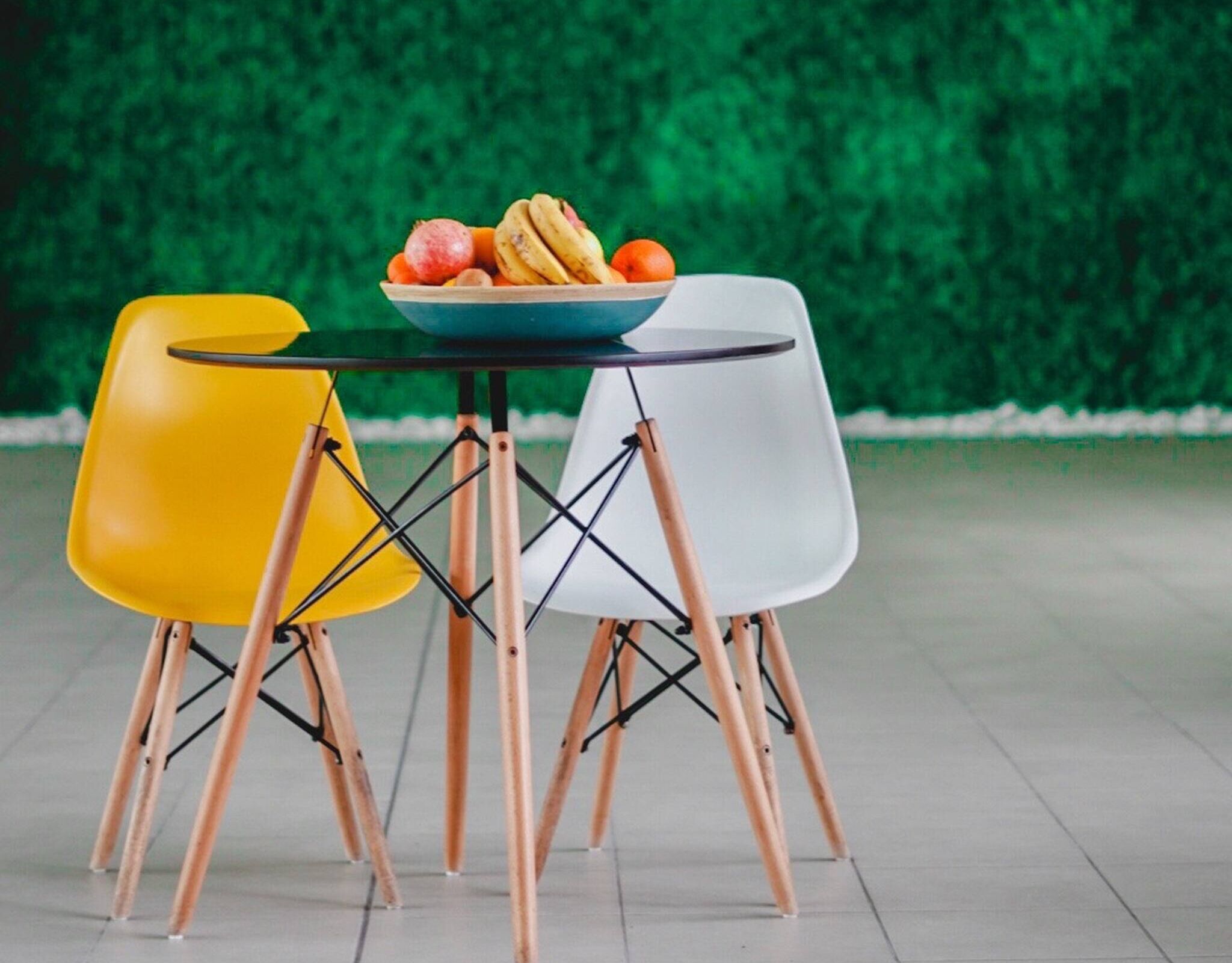 Een tafel met een schaal fruit en twee stoelen met houten poten.