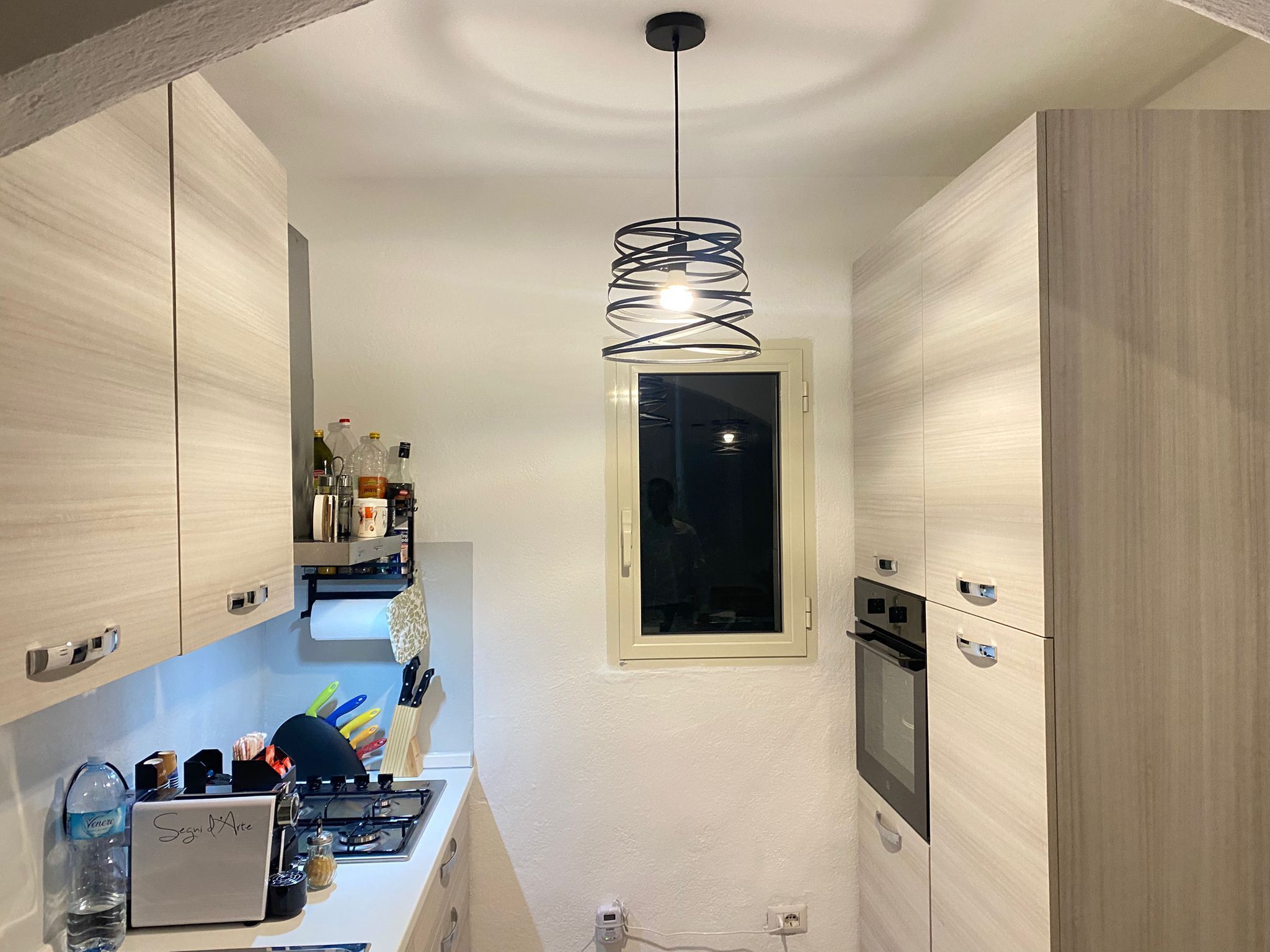 Een moderne keuken met houten kastjes, een gasfornuis, een inbouwoven en een hanglamp.