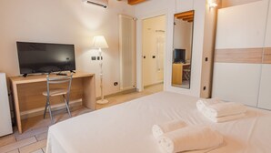 Ein Hotelzimmer mit einem Bett, einem Schreibtisch mit Stuhl, einem Fernseher, einer Lampe, einem Heizkörper und einem Kleiderschrank.