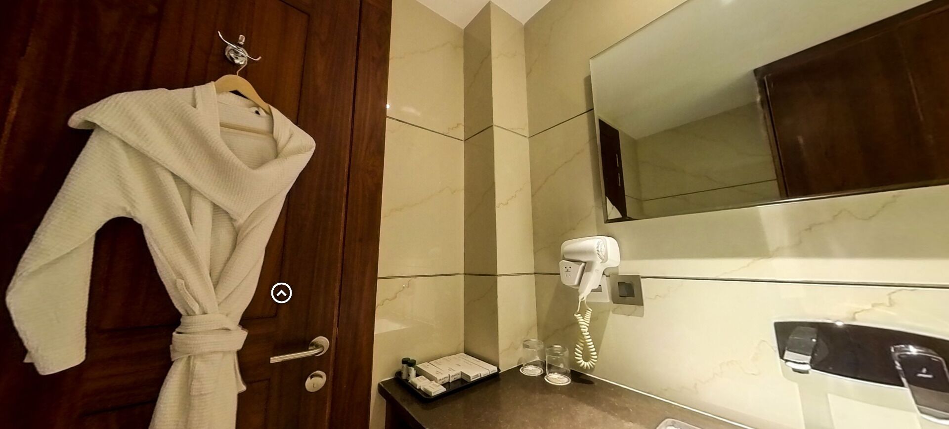 Un baño con puerta de madera, una bata blanca colgada en la puerta, un secador de pelo y un teléfono.