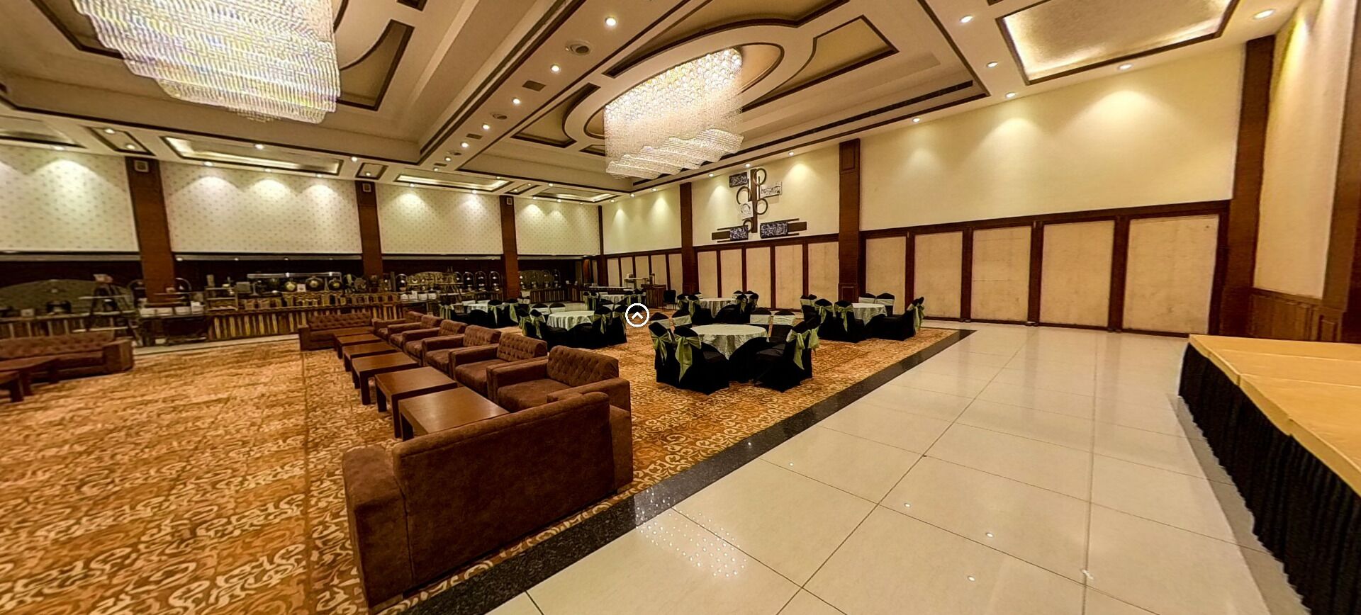 A spacious banquet hall with rows of tables and chairs, a patterned carpet, and a chandelier.