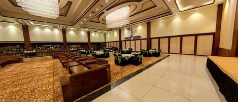 A spacious banquet hall with rows of tables and chairs, a patterned carpet, and a chandelier.
