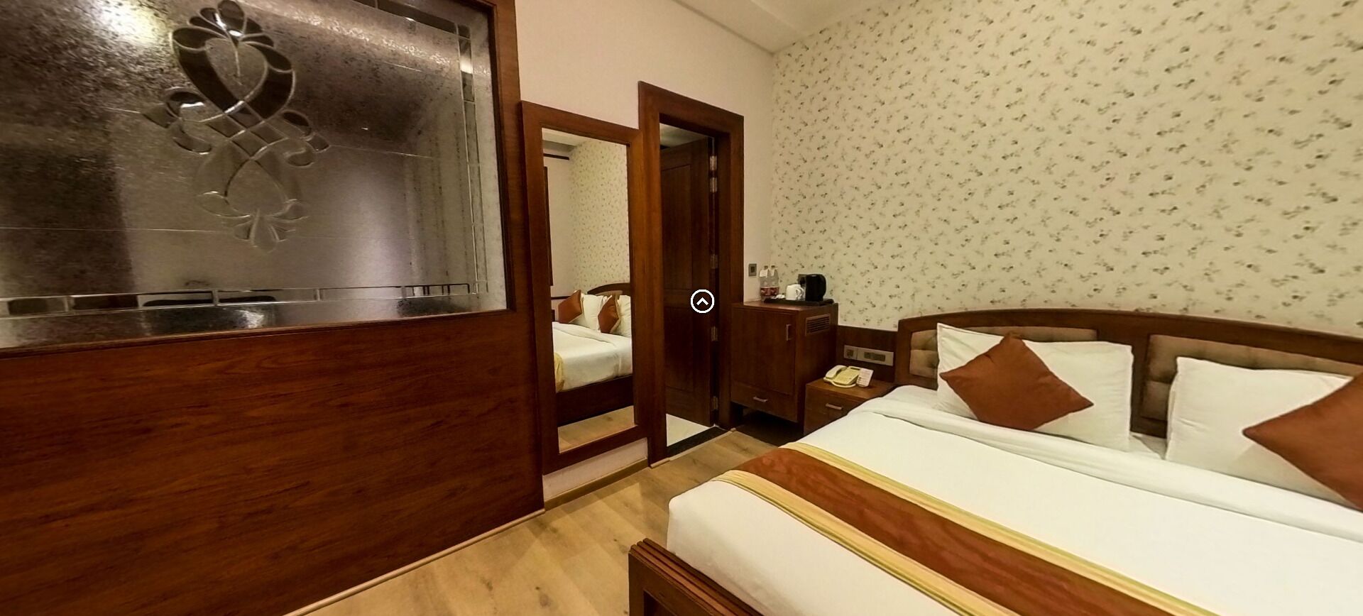 A hotel room with a bed, wooden headboard, a nightstand with a phone, and a mirror.