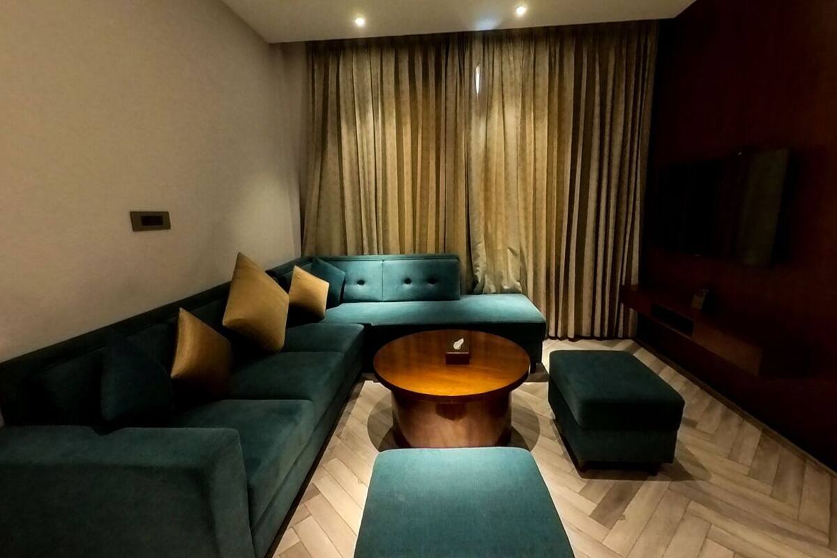Un salon moderne avec un canapé d’angle, une table basse ronde et un téléviseur fixé au mur.