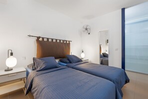 A hotel room with two beds, a bedside table, a nightstand, a wall-mounted fan, and a large mirror.