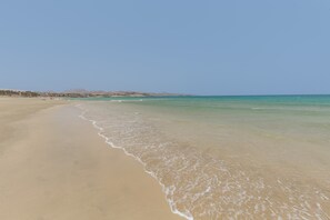 A beach with clear water, sandy shore, and distant hills.