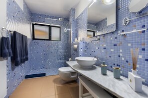 A bathroom with a tiled wall, a toilet, a sink with a basin, and a mirror.