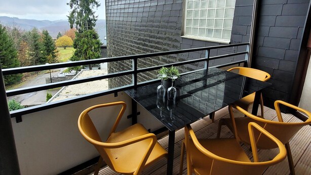 A balcony with a black table and four yellow chairs, overlooking a scenic view of trees and mountains. - Apartment in Winterberg Near Ski Lift (Winterberg)