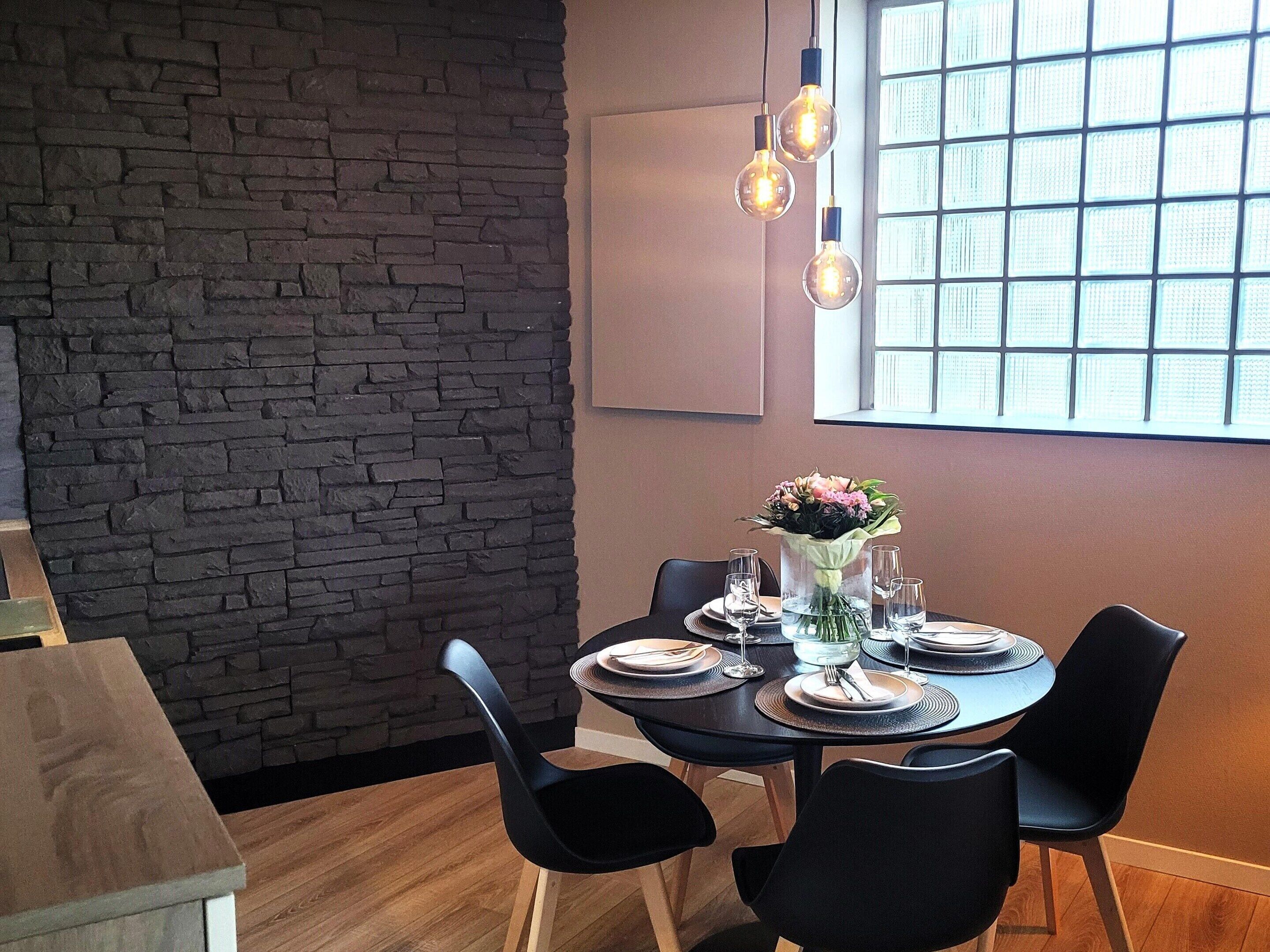 Un coin repas agrémenté d’un mur en pierre, une table ronde mise avec des assiettes, des verres et un vase de fleurs.