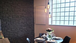 A dining area with a stone wall, a round table set with plates, glasses, and a vase of flowers. - Apartment in Winterberg Near Ski Lift (Winterberg)