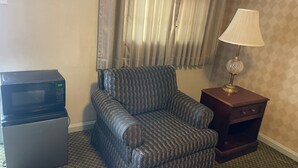 Ett hotellrum med en mikrovågsugn, en mönstrad fåtölj, en lampa och ett litet träbord som sängbord.