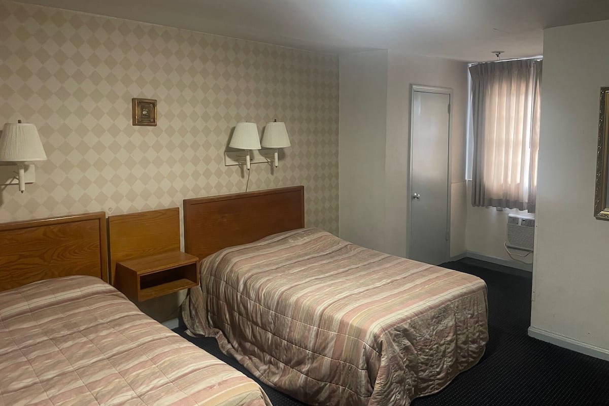 Habitación de hotel con dos camas, una mesita de noche, una lámpara, una puerta y una ventana con cortinas.