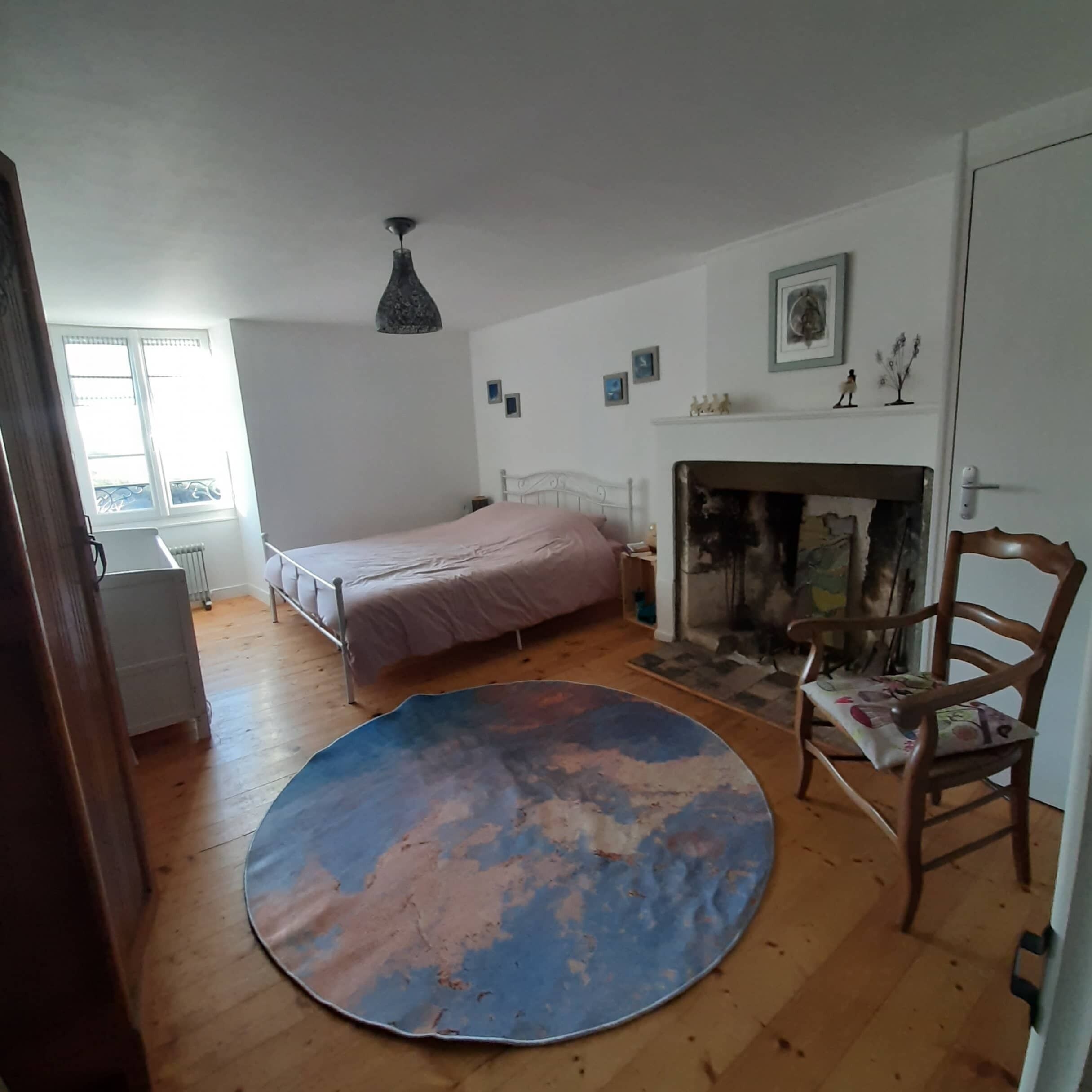 Un dormitorio con cama, chimenea, una silla y un tapete redondo.