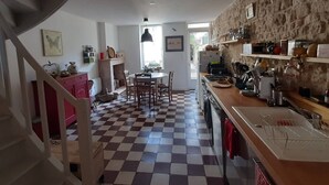 A kitchen with a checkered floor, a dining area, and a staircase leading to another level. - Gîte "La P'tite Jeannette", between land and sea, on the banks of the Charente. (Saint-Savinien)