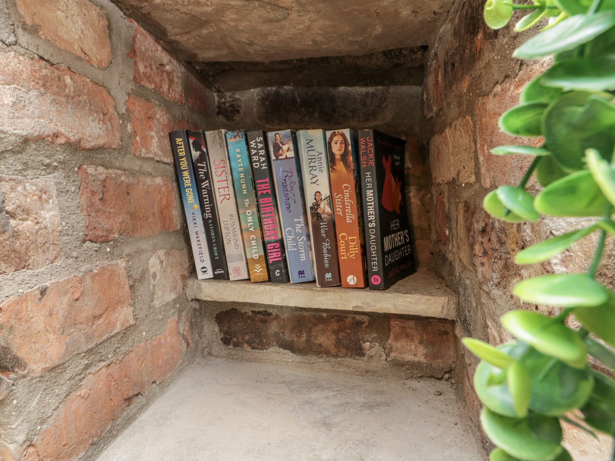 A shelf with a collection of books in a brick-walled alcove.
