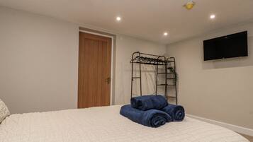 A bedroom with a bed, a wooden door, a black metal shelf, and a flat-screen TV on the wall.