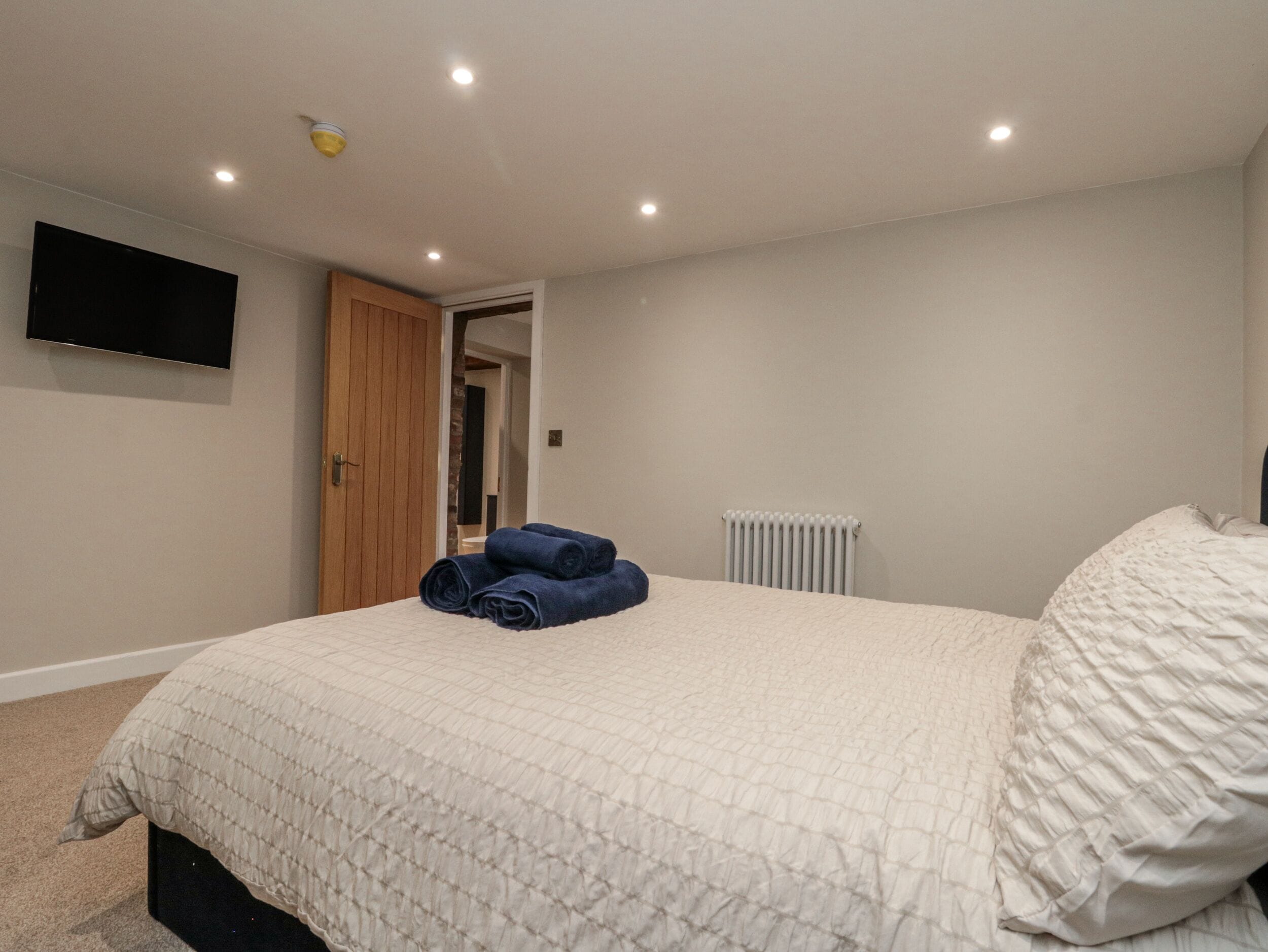 A bedroom with a bed, a flat-screen TV mounted on the wall, a wooden door, and a radiator.