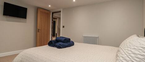 A bedroom with a bed, a flat-screen TV mounted on the wall, a wooden door, and a radiator.