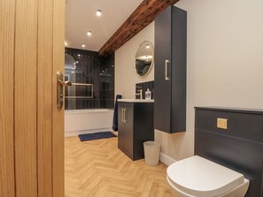 A modern bathroom with a wooden floor, a bathtub, a toilet, and a vanity with a mirror. - Betsy's Burrow (Bridlington)