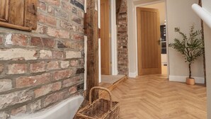 A hallway with a brick wall, wooden door, and a potted plant. - Betsy's Burrow (Bridlington)