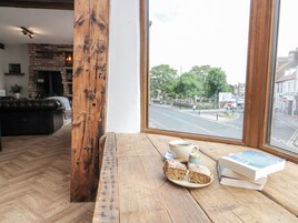 A wooden bench with a cup of coffee, a plate of cake, and books by a window overlooking a street.