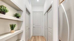 A narrow hallway with white walls, wooden flooring, and built-in shelving with potted plants. - This studio is a 0 bedroom(s), 1 bathrooms, located in Houston, TX. (Houston)