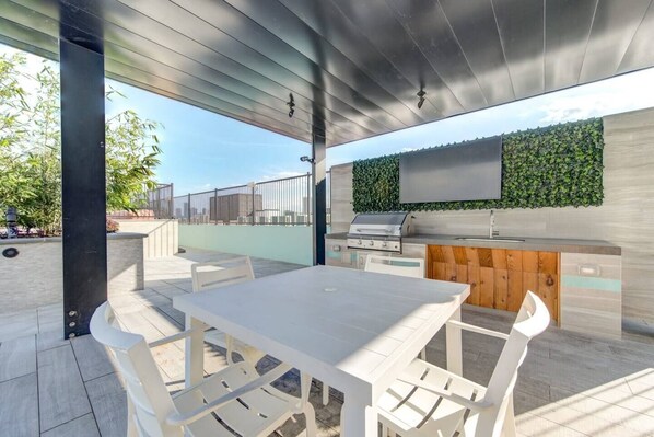 An outdoor patio with a white table and chairs, a built-in grill, and a vertical garden wall. - This inviting living space is the perfect spot to relax and unwind (Houston)