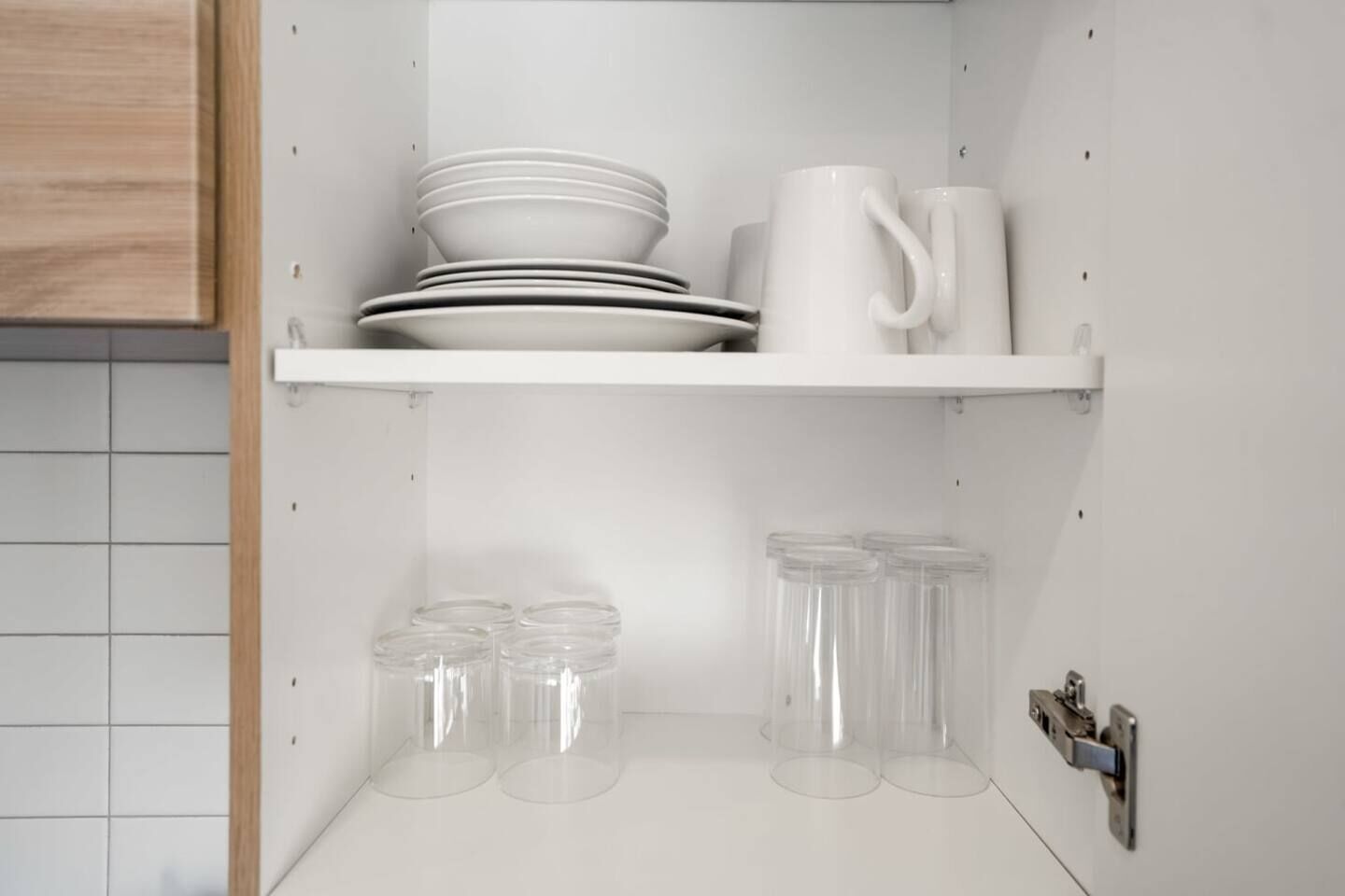 A kitchen with white cabinets, a white countertop, and a white shelf holding plates, a mug, and glass jars.