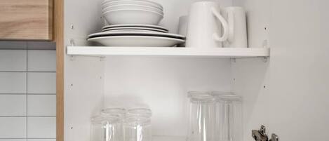 A kitchen with white cabinets, a white countertop, and a white shelf holding plates, a mug, and glass jars.