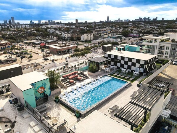 A rooftop pool area with lounge chairs and a checkered building nearby. - This inviting living space is the perfect spot to relax and unwind (Houston)