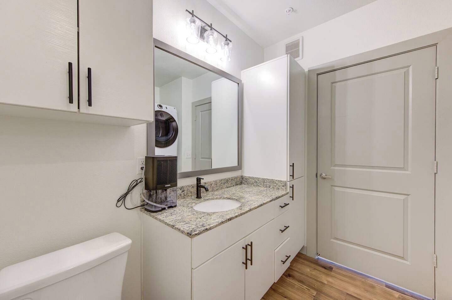 A bathroom with a white vanity, a sink, a mirror, a hair dryer, and a door.
