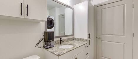 A bathroom with a white vanity, a sink, a mirror, a hair dryer, and a door.