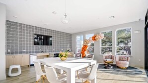 A modern kitchen with a geometric backsplash, a dining area with a white table and chairs, and a large window with a view of trees.