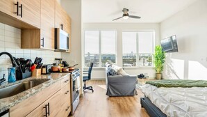 A modern apartment with a kitchen, a dining area, a living room with a sofa, a TV, and a large window with a city view.