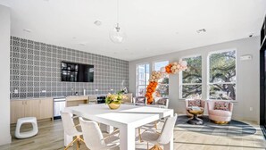 A modern kitchen with a geometric backsplash, a dining area with a white table and chairs, and a large window with a view of trees.