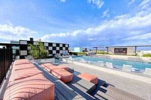 Un área de piscina en la azotea con sillones de descanso y un edificio moderno al fondo.