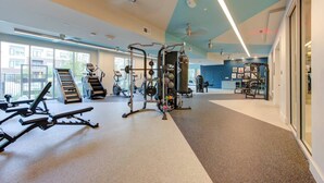 Une salle de sport moderne dotée de divers appareils d’entraînement, de grandes fenêtres et d’un aménagement propre et spacieux.