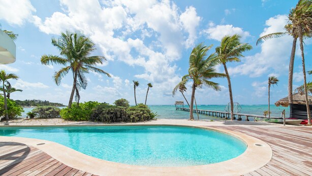 A wooden deck surrounding a clear blue pool with palm trees and a view of the ocean. - Charming 2-bedroom apartment in lovely Dreams Tulum (Dreams Tulum)