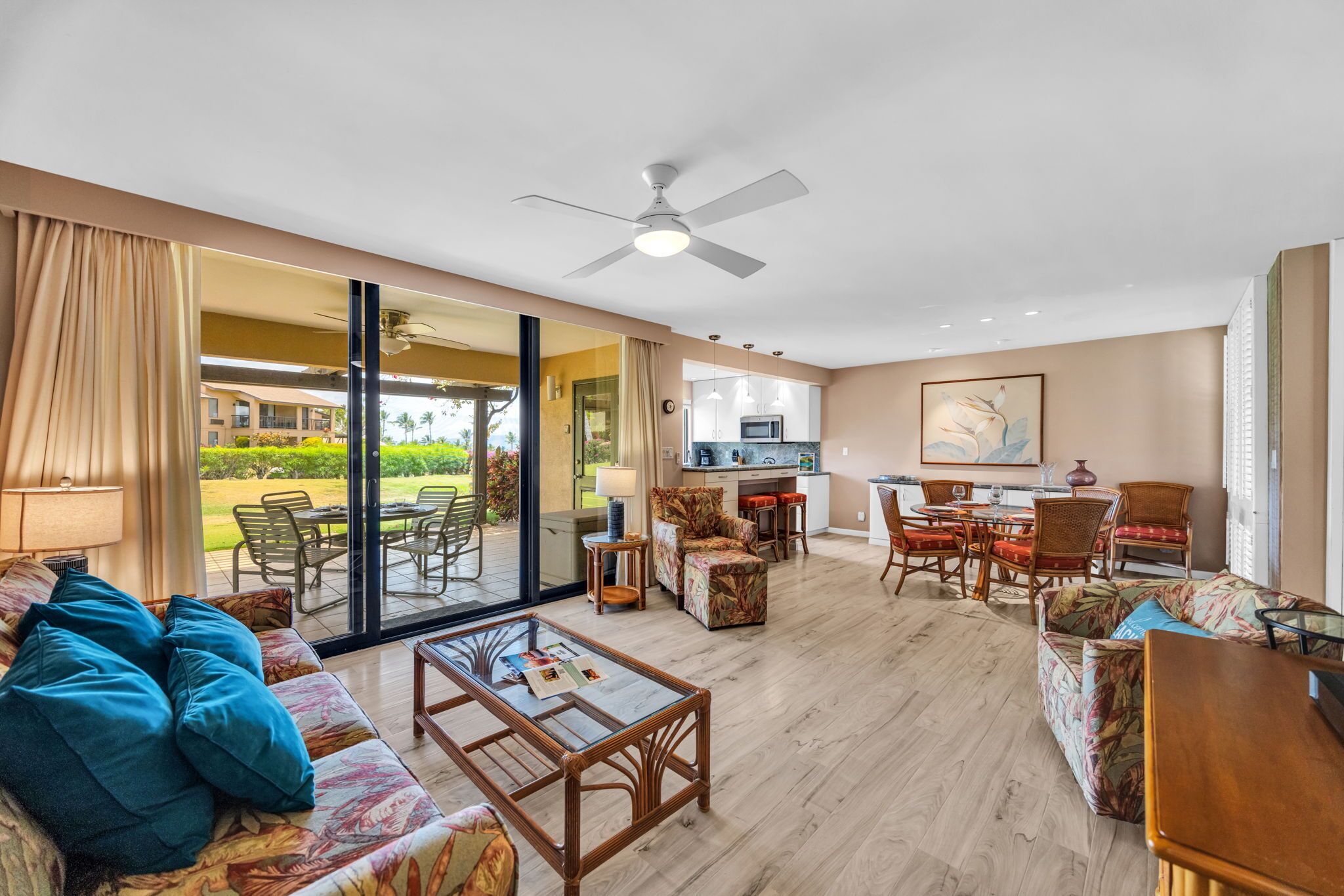 A spacious living area with a sofa, coffee table, and dining set. There is a sliding glass door leading to an outdoor patio.